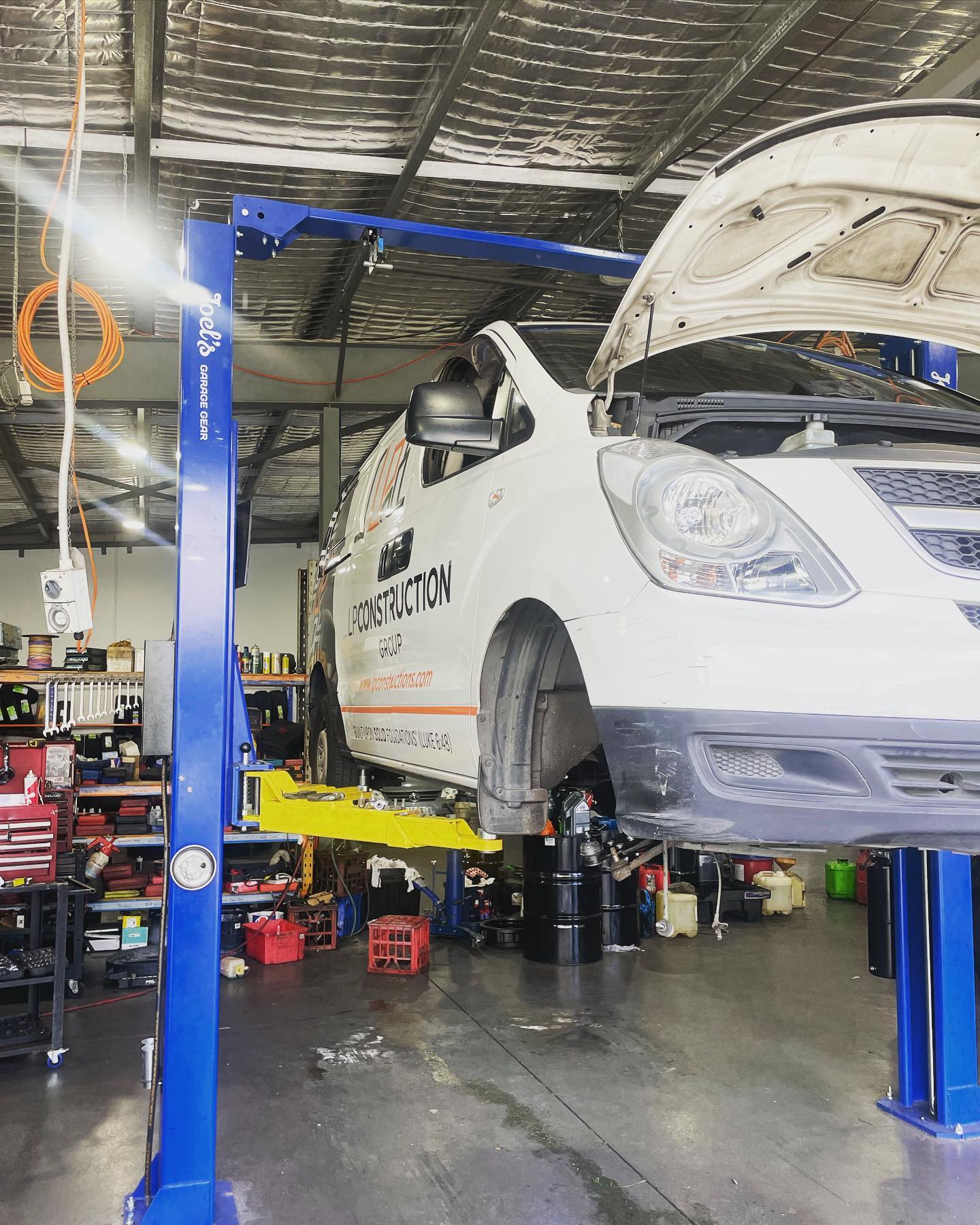 A van up on one of the blue two-post hoists inside the LP Automotive workshop, with the parts shelving behind